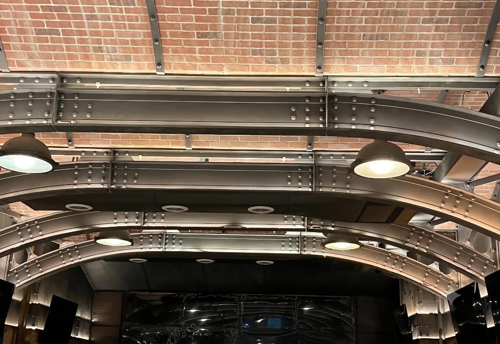 Arched riveted steel beams with pendant lights against exposed brick ceiling