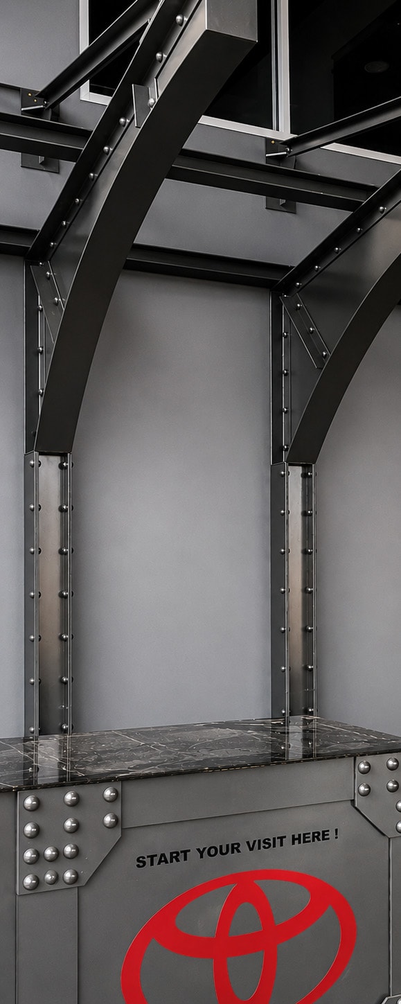 Toyota dealership reception desk with arched faux steel frame and riveted columns